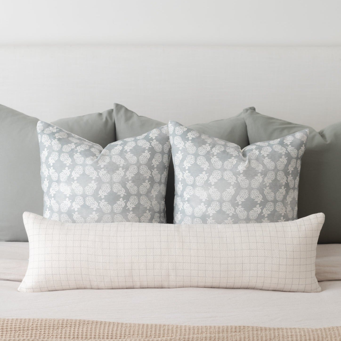 Cream-colored lumbar pillow with fine grid pattern, displayed with two gray patterned pillows on a bed.