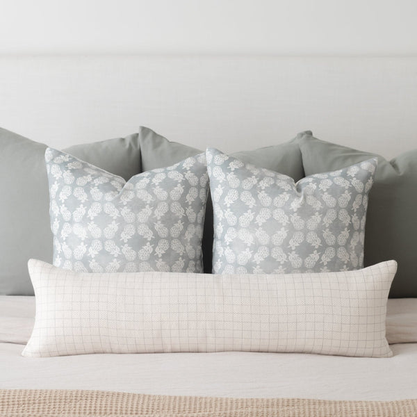 Cream-colored lumbar pillow with fine grid pattern, displayed with two gray patterned pillows on a bed.