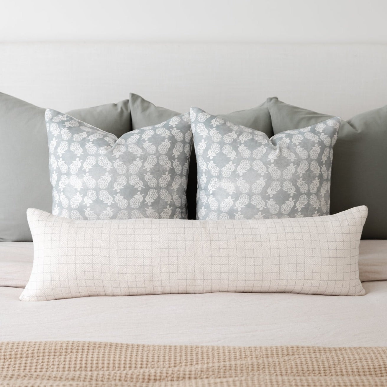 Rectangular lumbar pillow with light grid pattern in cream and beige tones, displayed with patterned and solid pillows on a b