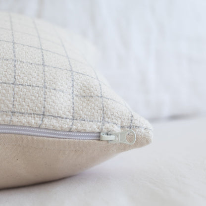 Cream lumbar pillow with grid pattern and beige underside, featuring a concealed zipper closure.