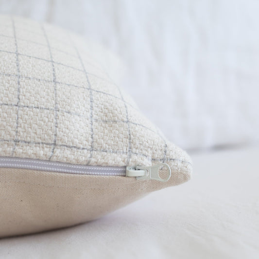 Cream lumbar pillow with grid pattern and beige underside, featuring a concealed zipper closure.
