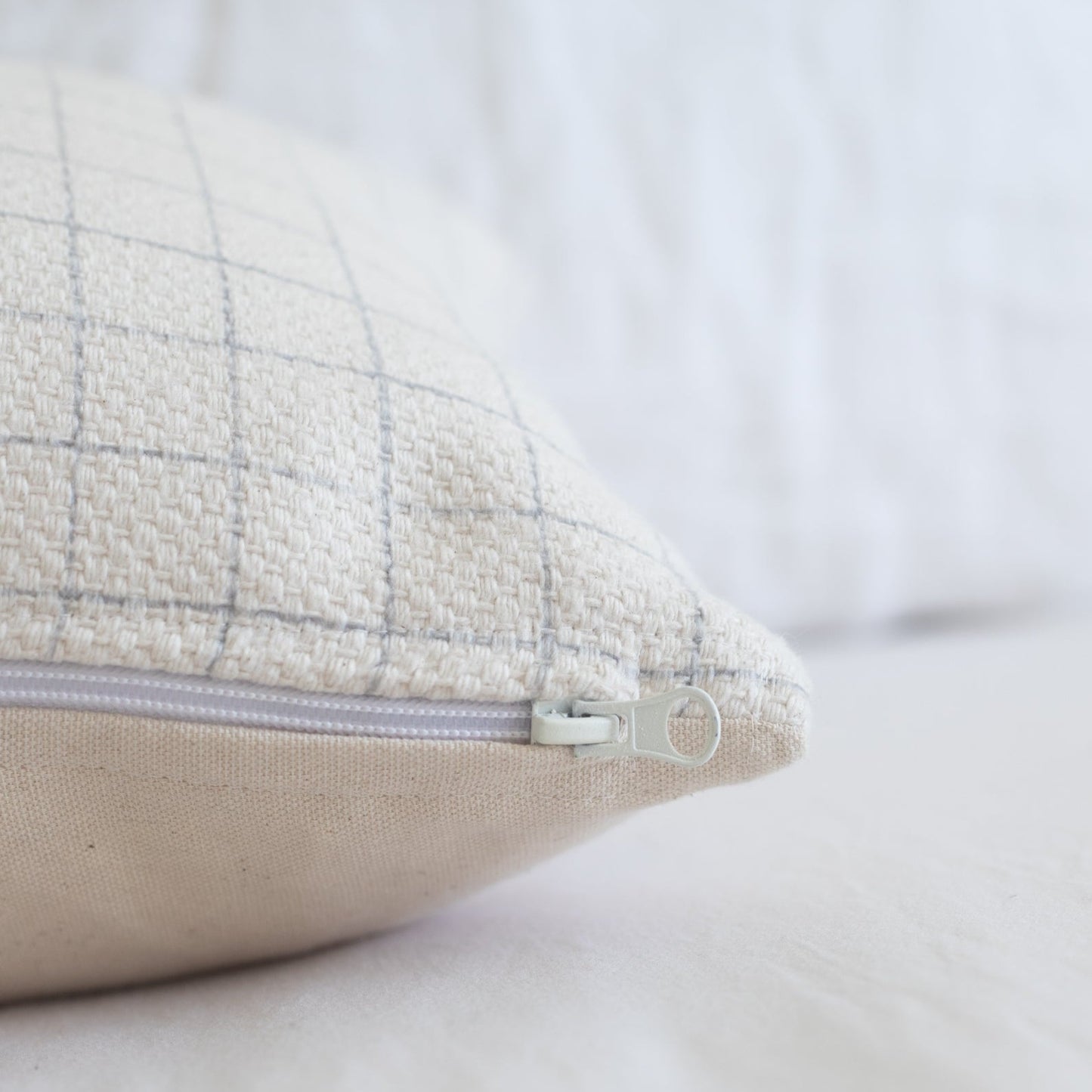 Cream and gray grid patterned pillow cover with lavender zipper, shown at an angle.