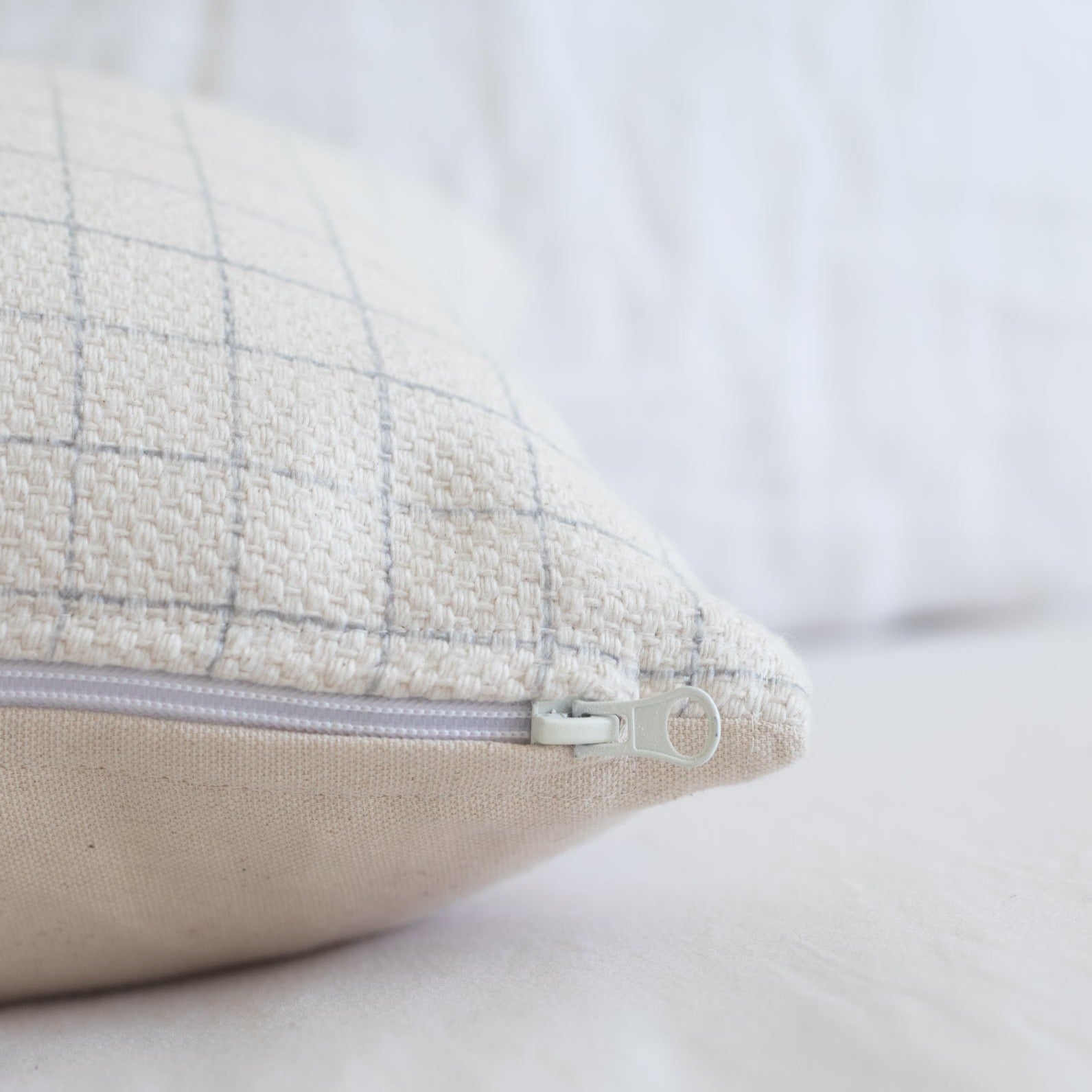Cream and gray grid patterned pillow cover with lavender zipper, shown at an angle.