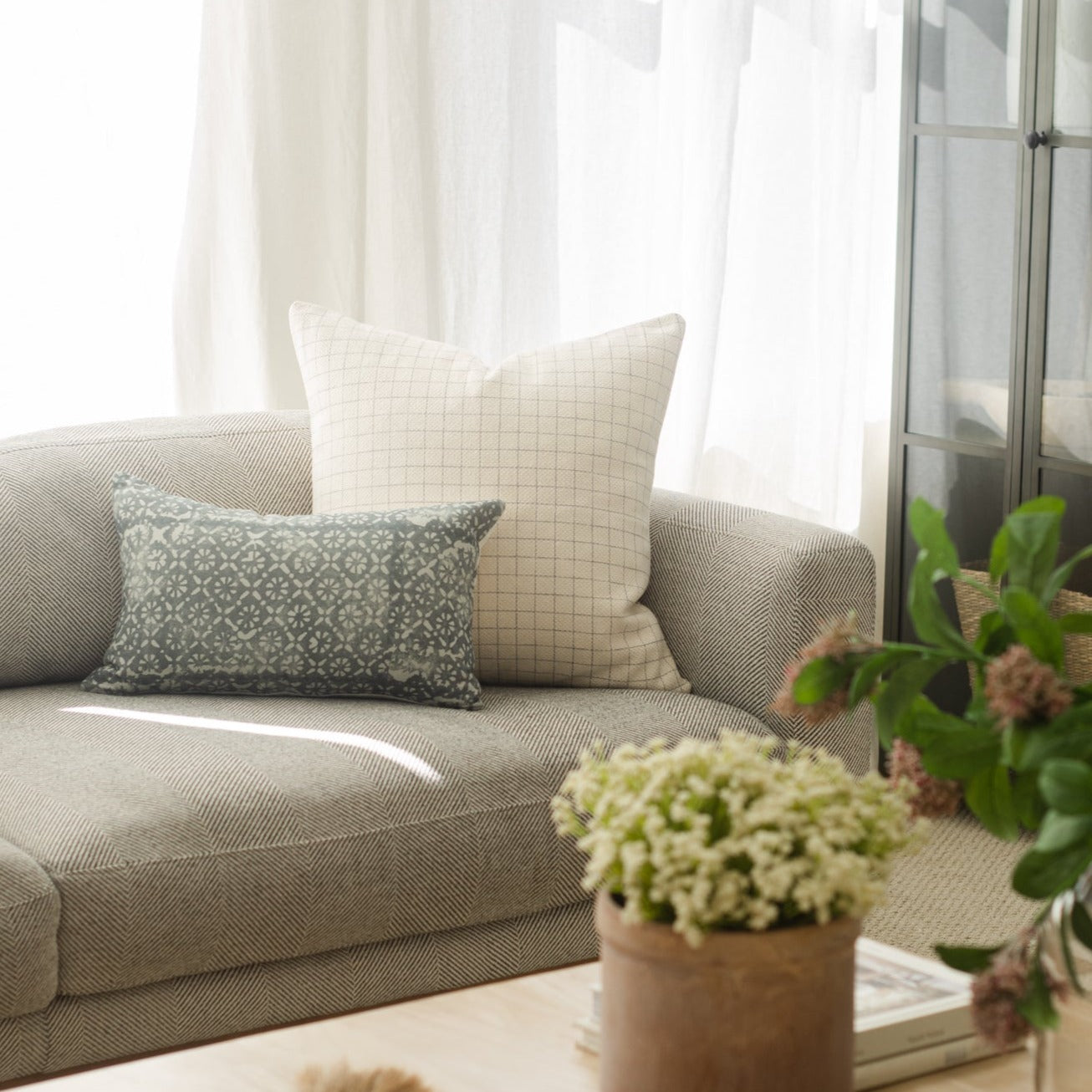 Cream grid patterned square pillow displayed on a beige sofa with patterned throw pillows.