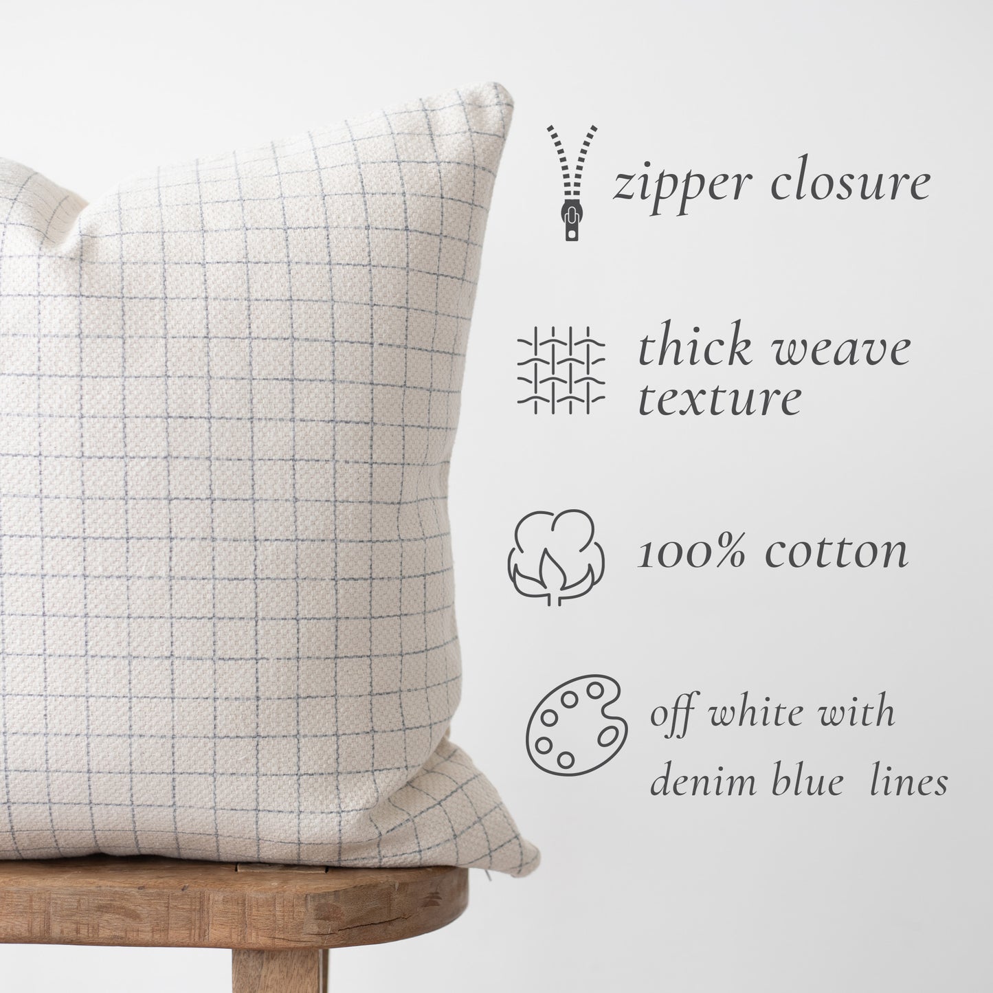 Off-white cotton grid pillow with denim blue lines, zipper closure, displayed on wooden stool.