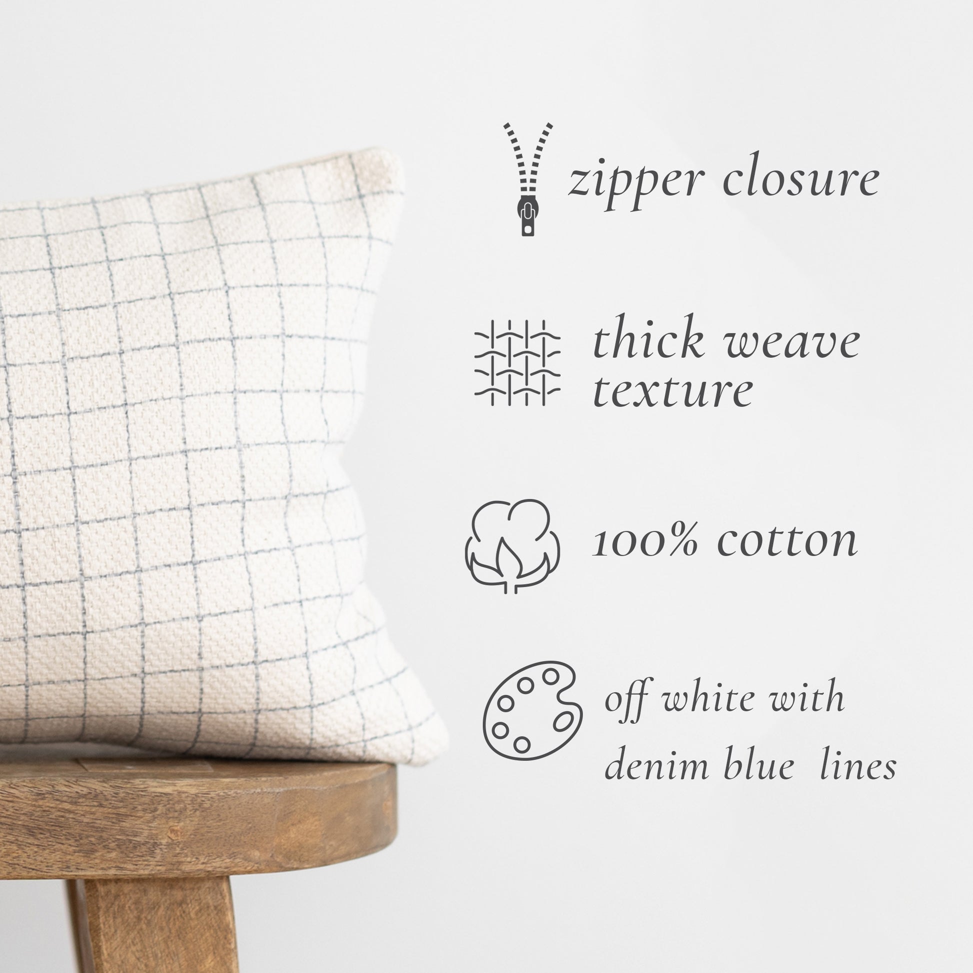 Off-white cotton lumbar pillow with denim blue grid pattern and zipper closure, displayed on wooden stool.