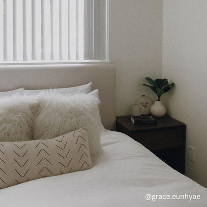 Beige lumbar pillow with chevron pattern displayed on bed with white pillows and bedding.